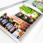 Image of the inside of a 555L large white display chest freezer with frozen goods, lid open.